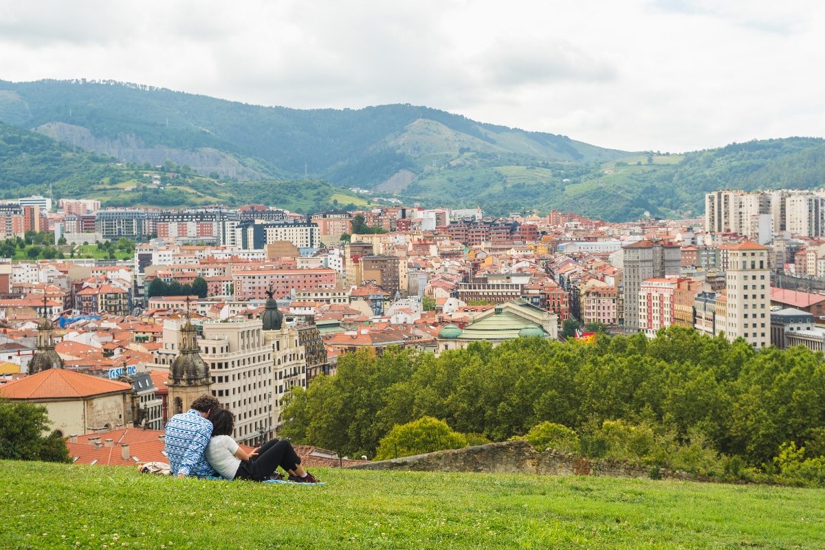 Una pareja tirada en la hierba con Bilbao de fondo.