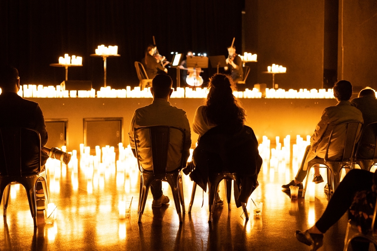 Personas sentadas en sillas y rodeadas de velas encendidas mientras miran el escenario